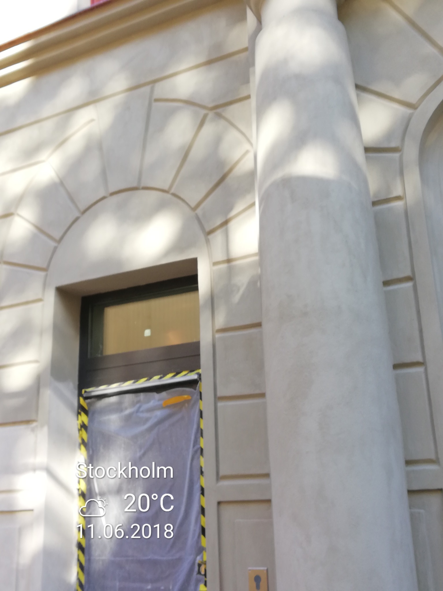 Elewacja budynku z kolumną, detalami architektonicznymi i zabezpieczonym wejściem, prawdopodobnie w trakcie prac wykończeniowych.