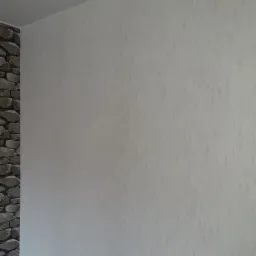 Ściana z dekoracyjną strukturą i fragmentem imitacji kamienia w rogu, jasne oświetlenie