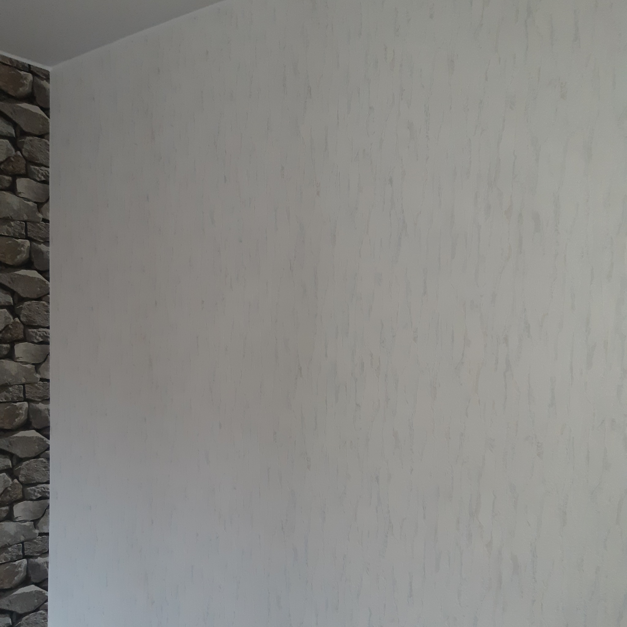 Ściana z dekoracyjną strukturą i fragmentem imitacji kamienia w rogu, jasne oświetlenie