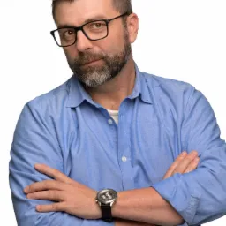 Portret mężczyzny w okularach i niebieskiej koszuli z założonymi rękami, prezentującego się profesjonalnie.