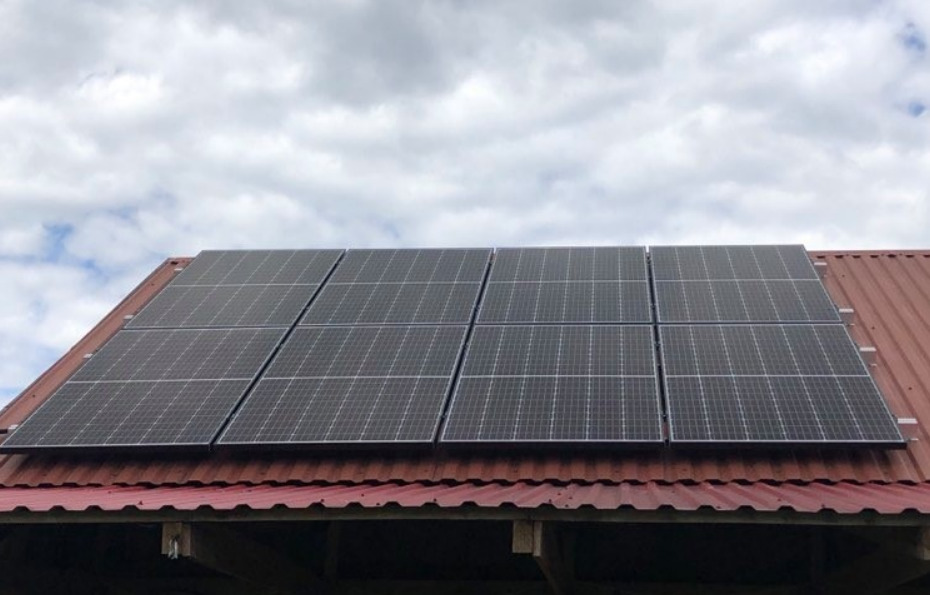 Panel słoneczny 2x4 na czerwonym, blaszanym dachu budynku gospodarczego, pochmurne niebo w tle.