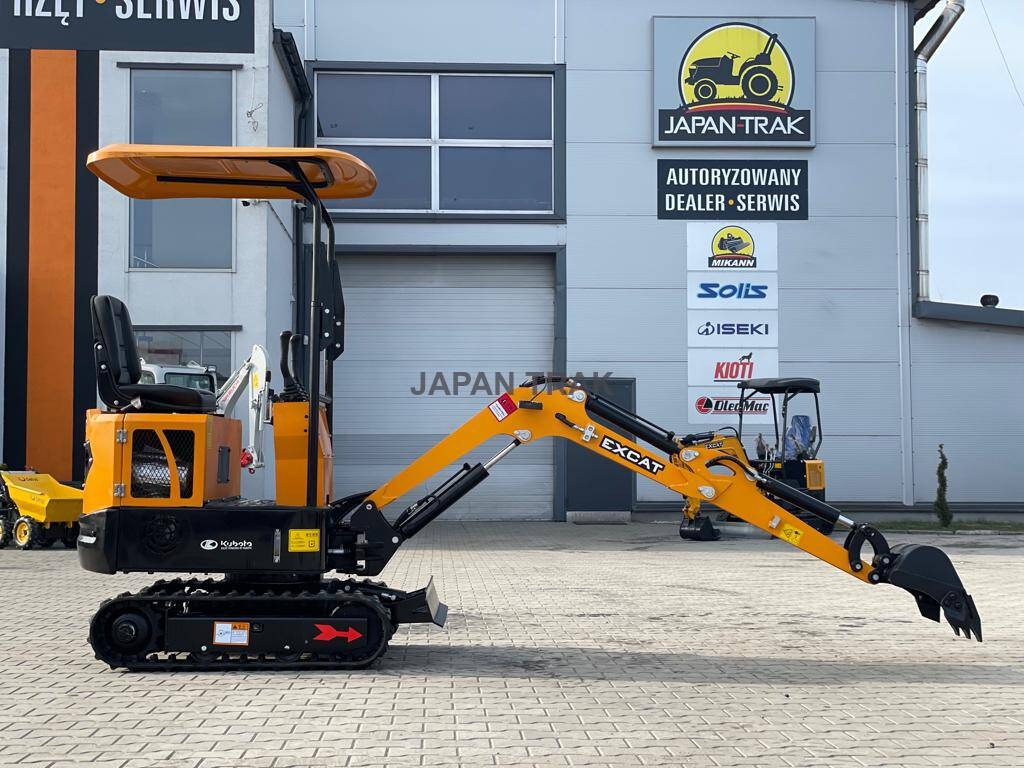 Żółto-czarna minikoparka marki Kubota EXCAT na gąsienicach, prezentowana na tle budynku autoryzowanego dealera Japan Trak z widocznymi logotypami Mikann, Solis, Iseki, Kioti i Oleo-Mac.