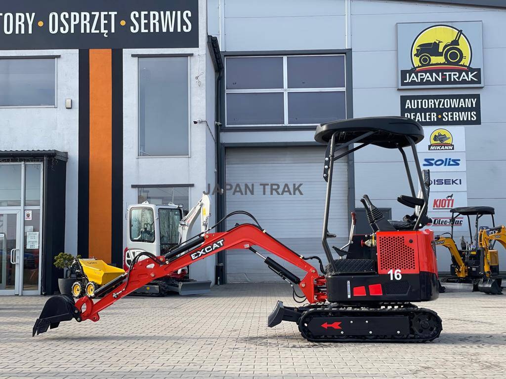 Czerwono-czarna minikoparka EXCAT z wysięgnikiem na tle budynku firmy Japan Trak z logo i informacją o autoryzowanym serwisie, inne maszyny budowlane w tle.
