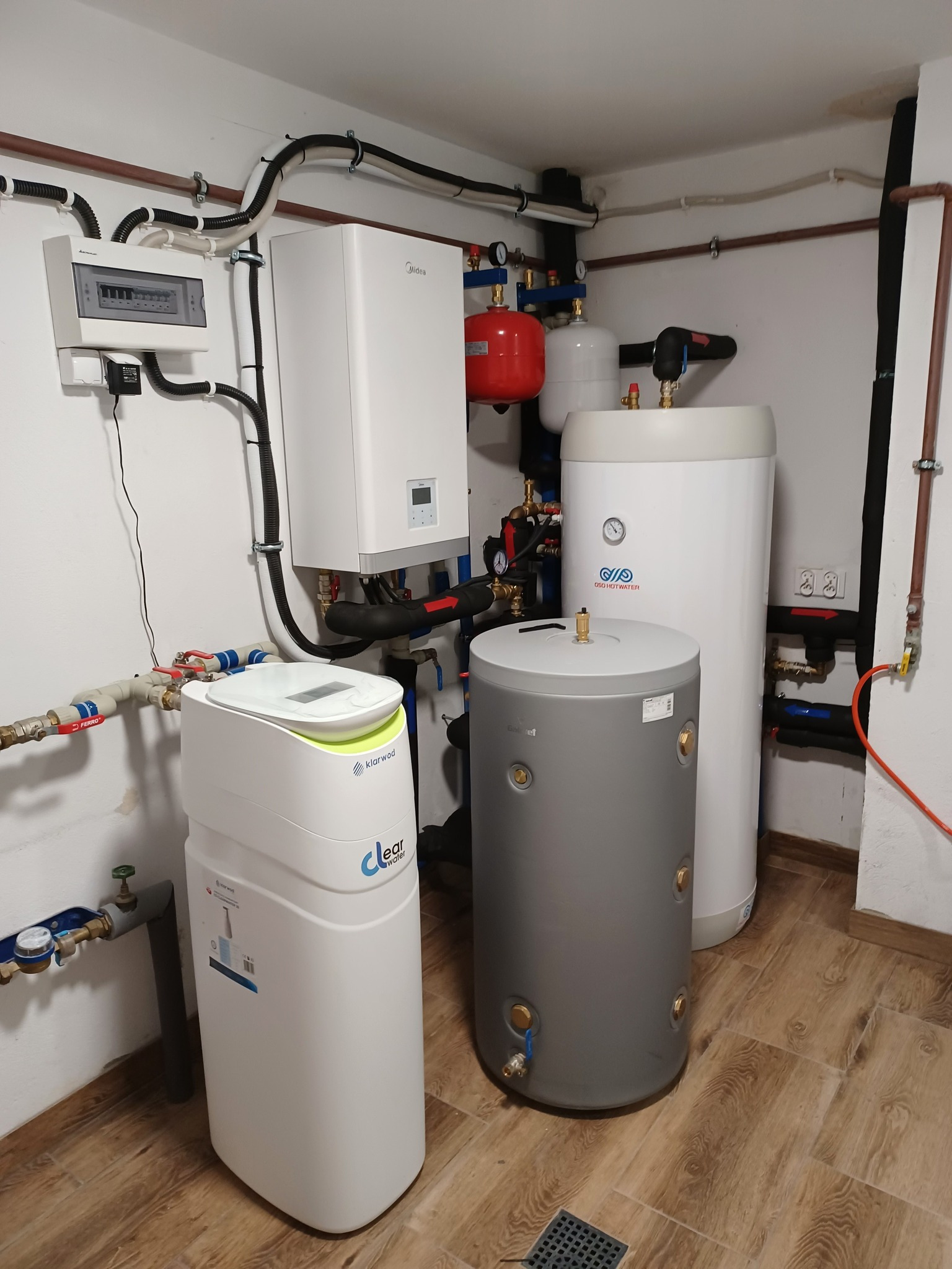 Kompletna kotłownia z pompą ciepła, zbiornikami buforowymi i zmiękczaczem wody Klarwod Clear Water, widoczne liczne rury i zawory, instalacja elektryczna na ścianie, podłoga wyłożona płytkami...