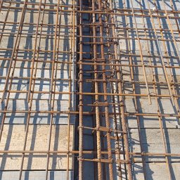 Uslugi budowlane Wacław smoter - Siatka zbrojeniowa ułożona na drewnianym szalunku, przygotowana do zalania betonem, widoczne pionowe pręty zbrojeniowe połączone drutem.