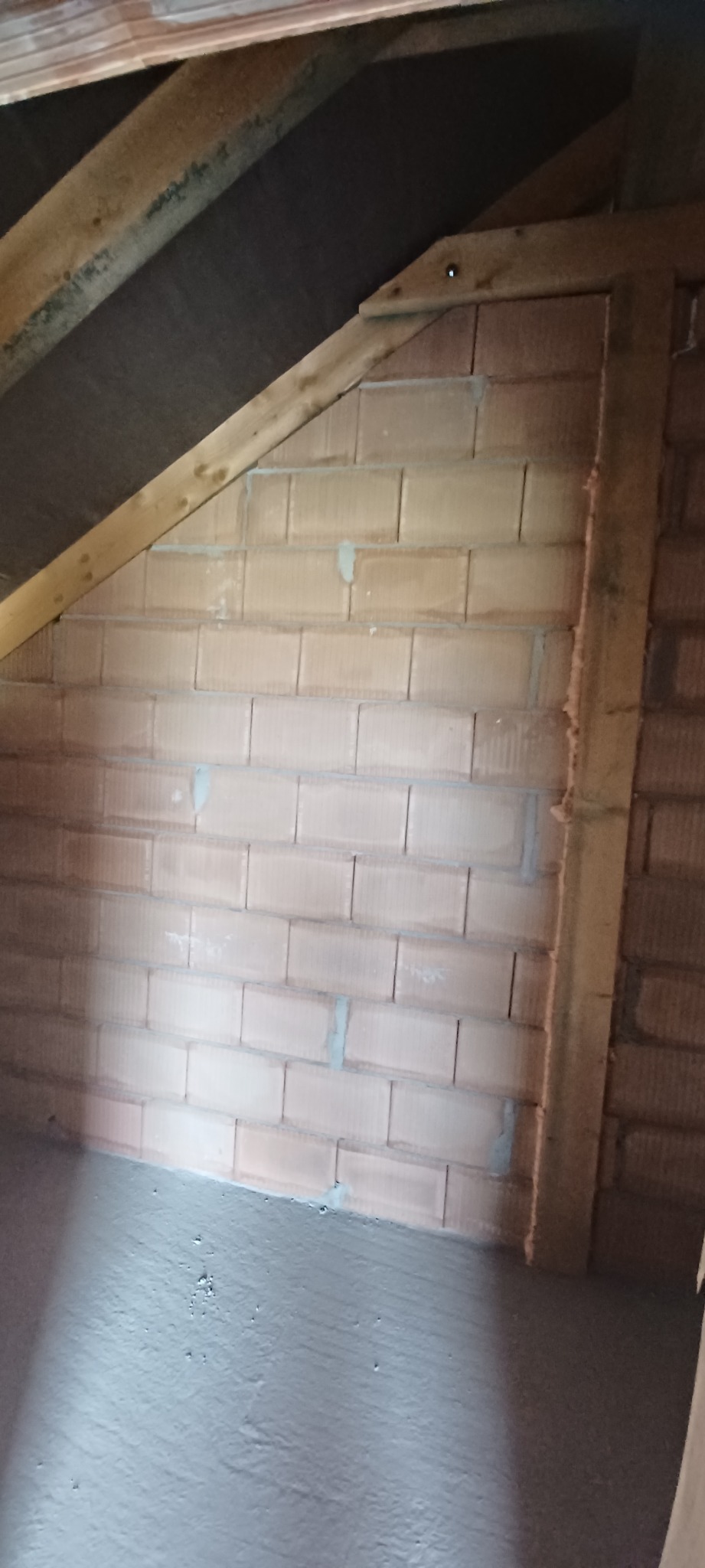 Ściana z bloczków ceramicznych w trakcie murowania z widocznymi spoinami, drewniana konstrukcja stropu oraz wylewka betonowa podłogi.