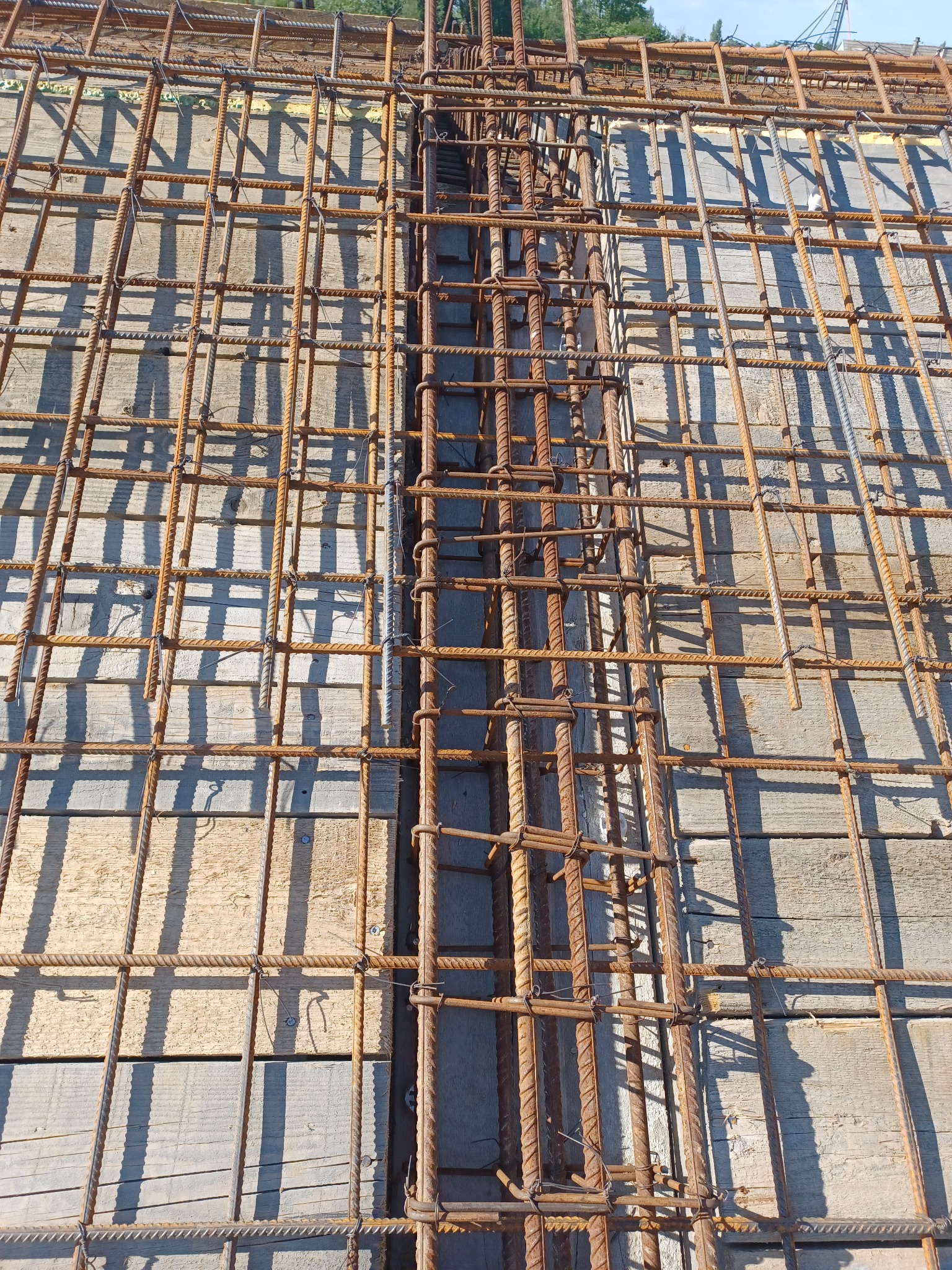 Siatka zbrojeniowa ułożona na drewnianym szalunku, przygotowana do zalania betonem, widoczne pionowe pręty zbrojeniowe połączone drutem.