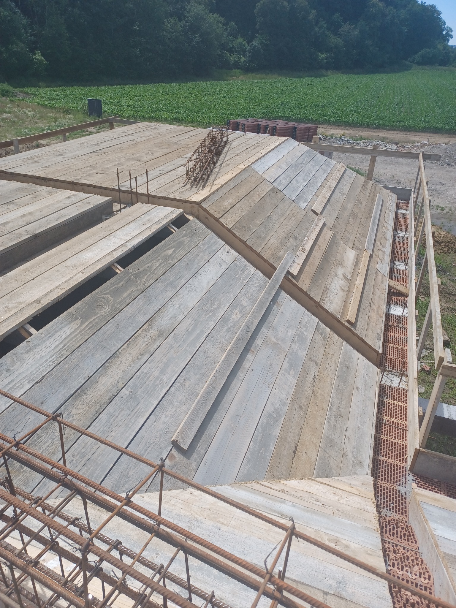 Szare, drewniane szalunki fundamentów zbrojonych stalą, przygotowane do zalania betonem w Wieliczce, z widocznym tłem zielonego pola i lasu.