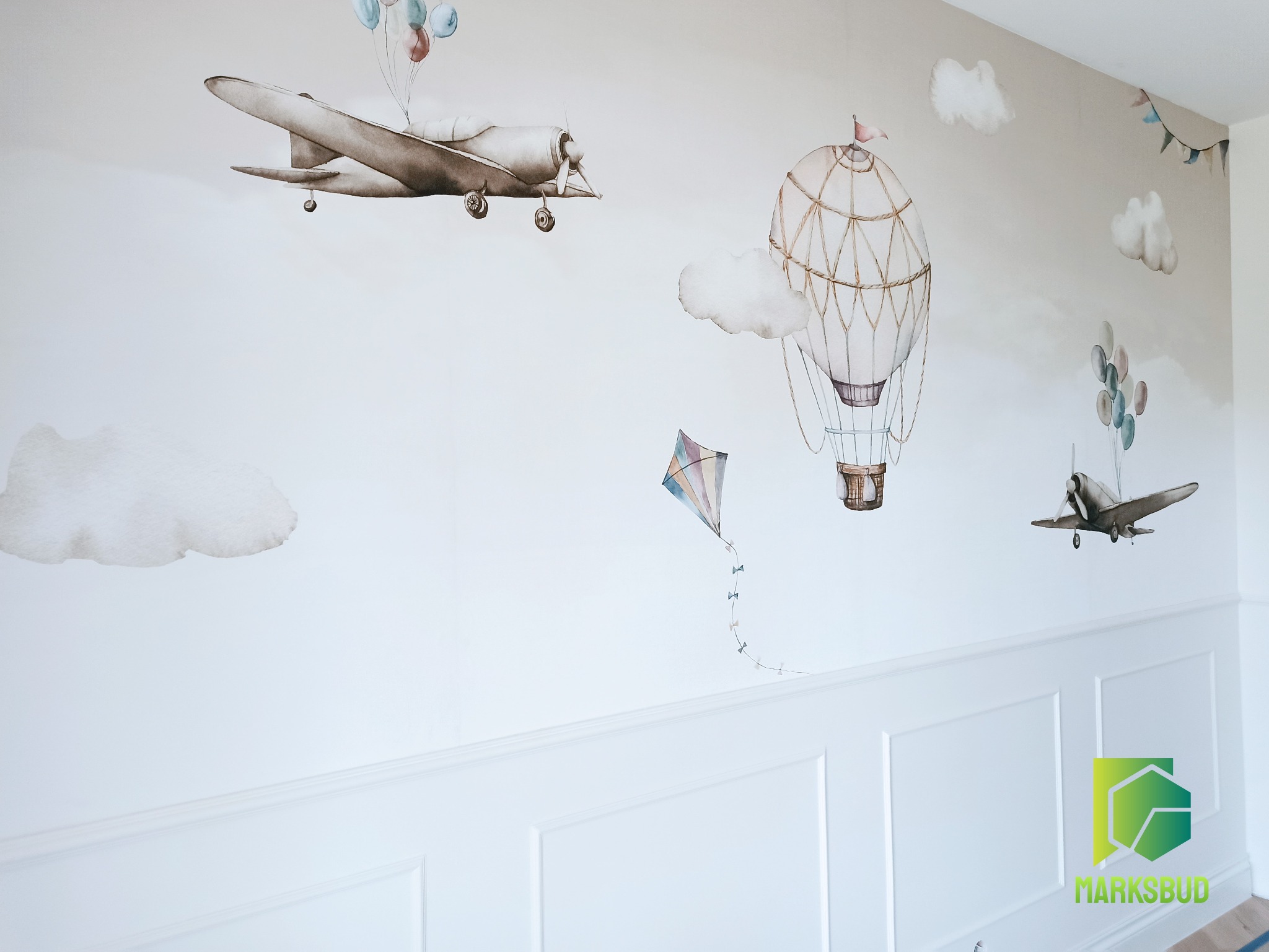 Dziecięcy pokój z dekoracyjną ścianą: akwarelowe malunki samolotów, balonu i latawca na białym tle z białą lamperią.