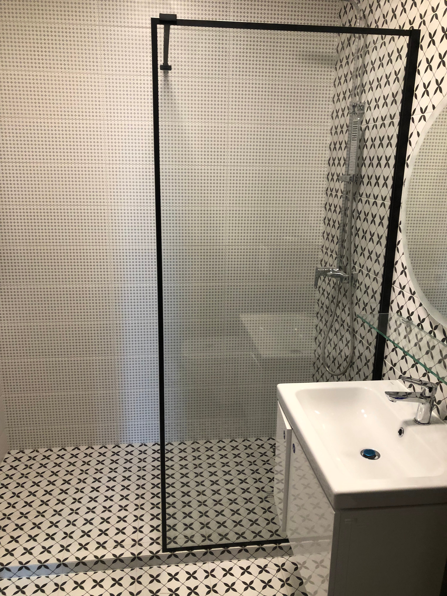 Nowoczesna łazienka z kabiną prysznicową w czarnej ramie, umywalką z szafką i wzorzystymi płytkami podłogowymi i ściennymi.