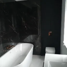 Nowoczesna łazienka z czarnymi marmurowymi płytkami, białą wanną wolnostojącą, wiszącą toaletą i umywalką nablatową.