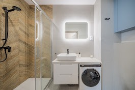 Nowoczesna łazienka z kabiną prysznicową typu walk-in, umywalką nablatową na szafce z pralką i podświetlanym lustrem. Ściana z wzorem jodełki.