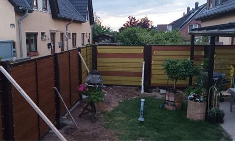 Montaż dwukolorowego ogrodzenia z paneli kompozytowych: brązowe pionowe panele z przodu i poziome żółto-brązowe z tyłu, w tle dom jednorodzinny i elementy zagospodarowania ogrodu.