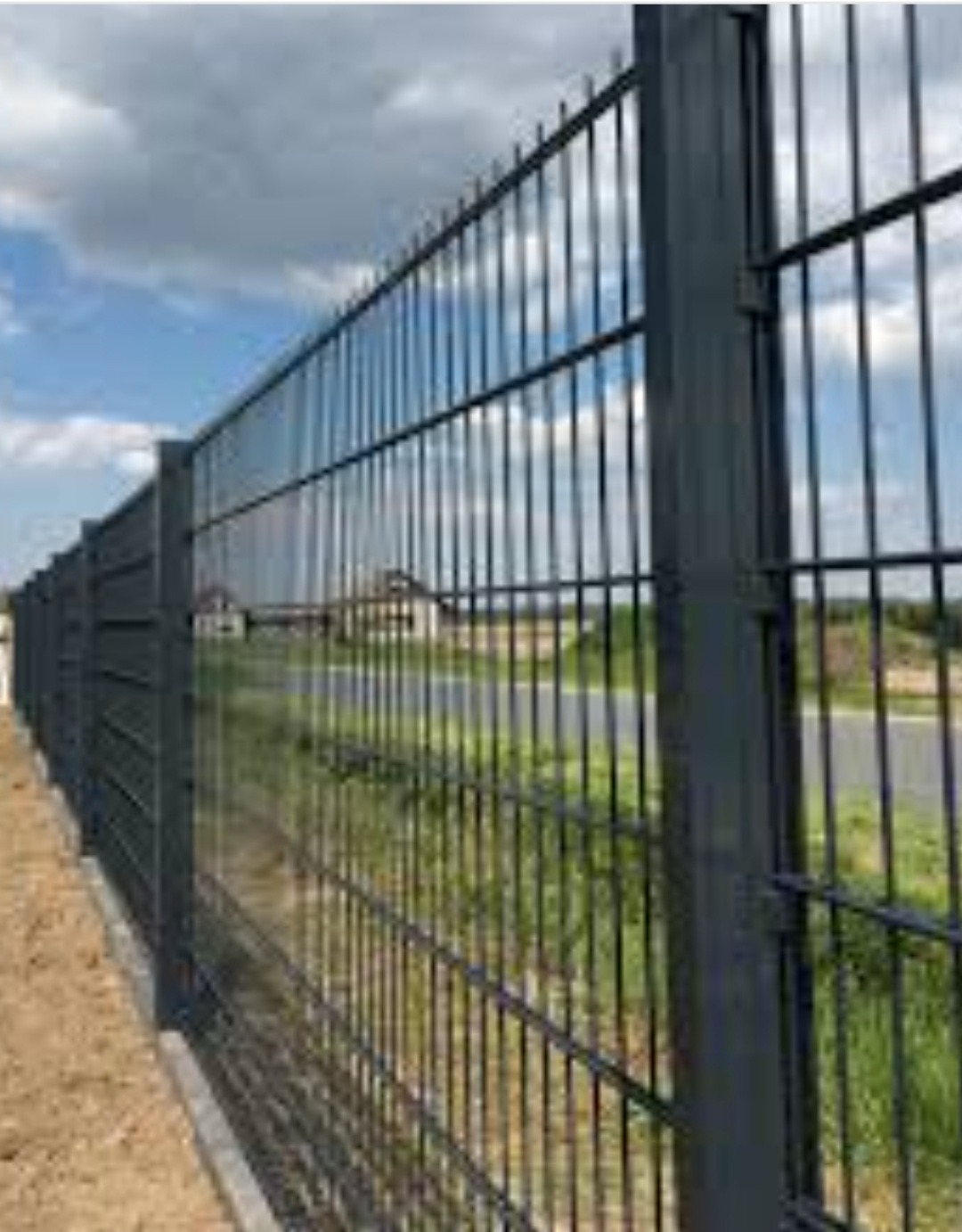 Nowoczesne, grafitowe ogrodzenie panelowe z grubych prętów, zamontowane w Kamieniu Małym, widoczne na tle zieleni i błękitnego nieba z chmurami.