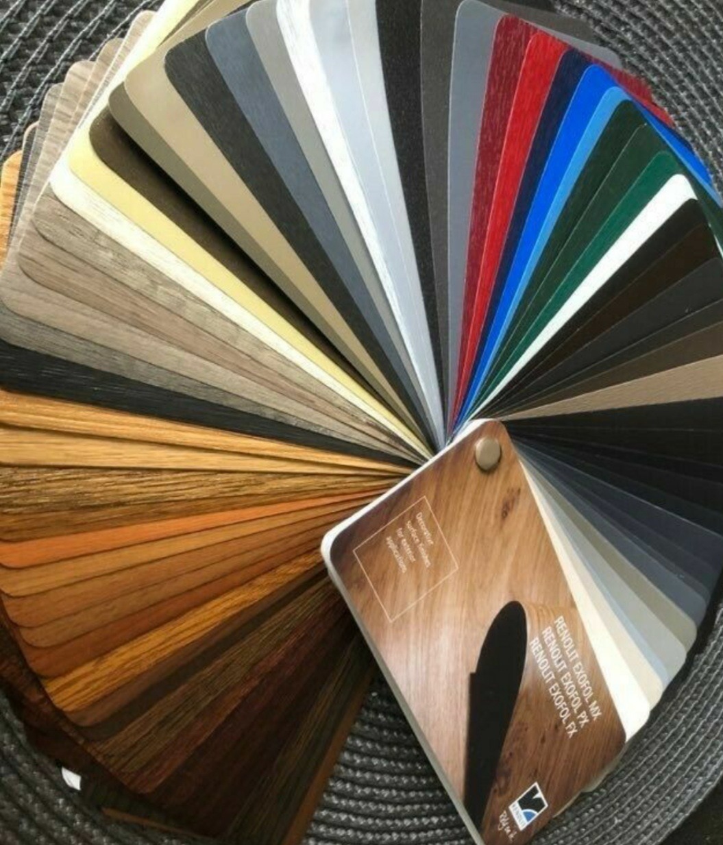 Katalog próbek kolorystycznych i faktur materiałów wykończeniowych, w tym drewnopodobnych i metalicznych, ułożonych wachlarzowo na szarym tle.