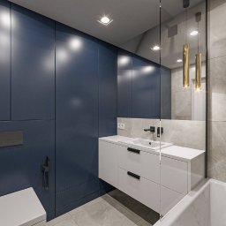 NOWA HATA SPÓŁKA Z OGRANICZONĄ ODPOWIEDZIALNOŚCIĄ - Nowoczesna łazienka z granatową zabudową, białą umywalką i szarą marmurową płytką. Złote lampy wiszące dodają elegancji.