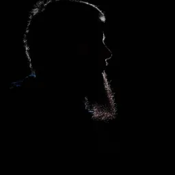 Sylwetka mężczyzny z brodą oświetlona od tyłu, ukazująca kontury włosów i brody na czarnym tle.