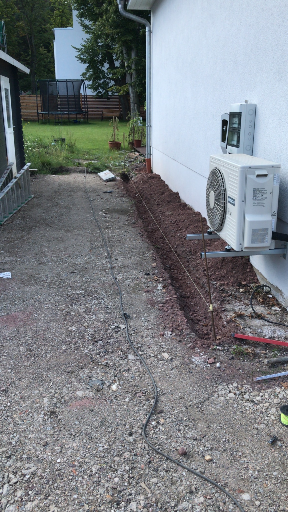 Wykop wzdłuż ściany budynku, przygotowany pod instalację odwodnienia liniowego, z widocznym agregatem klimatyzacji i kablem zasilającym.