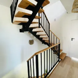 Nowoczesne schody metalowe z drewnianymi stopniami i czarną balustradą, widok z góry, minimalistyczny design wnętrza z białymi ścianami.