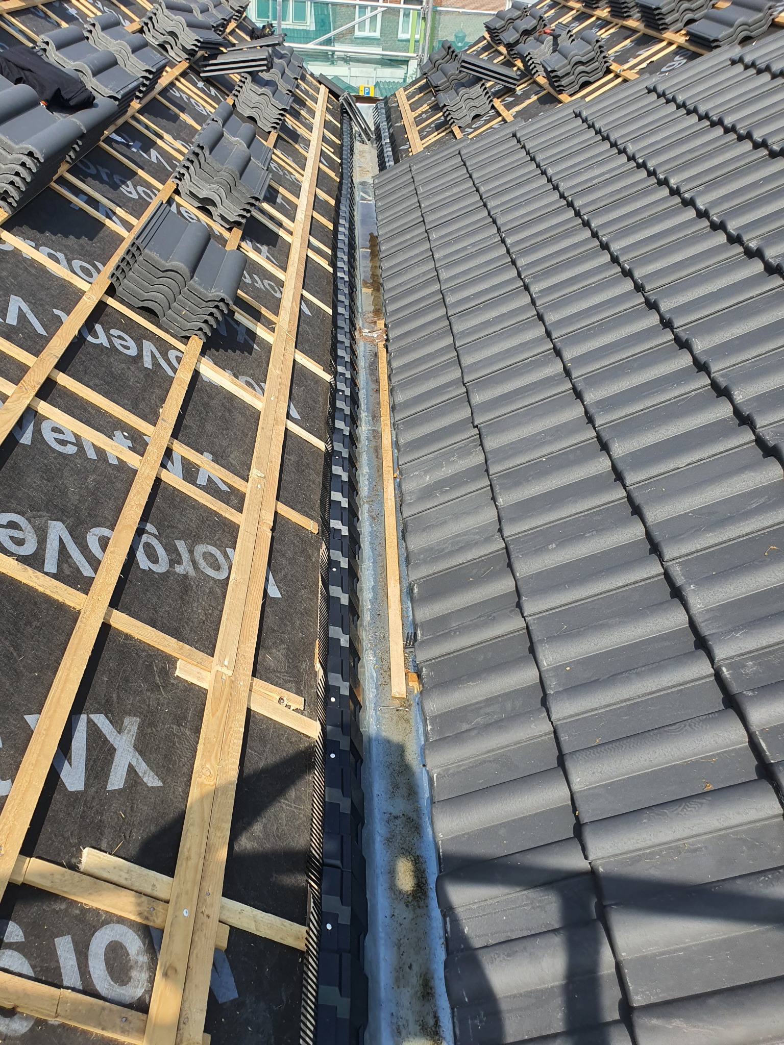 Fragment dachu z widoczną konstrukcją drewnianą, membraną dachową i ułożoną częścią szarej dachówki ceramicznej.