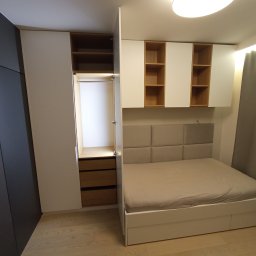 Dakon Daniel Kondzior - Nowoczesna sypialnia z zabudową meblową: szafa wnękowa z drewnianymi szufladami, białe szafki wiszące z otwartymi półkami z jasnego drewna oraz łóżko z tapicerowanym zagłówkiem w odcieniach beżu.