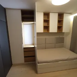 Nowoczesna sypialnia z zabudową meblową: szafa wnękowa z drewnianymi szufladami, białe szafki wiszące z otwartymi półkami z jasnego drewna oraz łóżko z tapicerowanym zagłówkiem w odcieniach beżu.