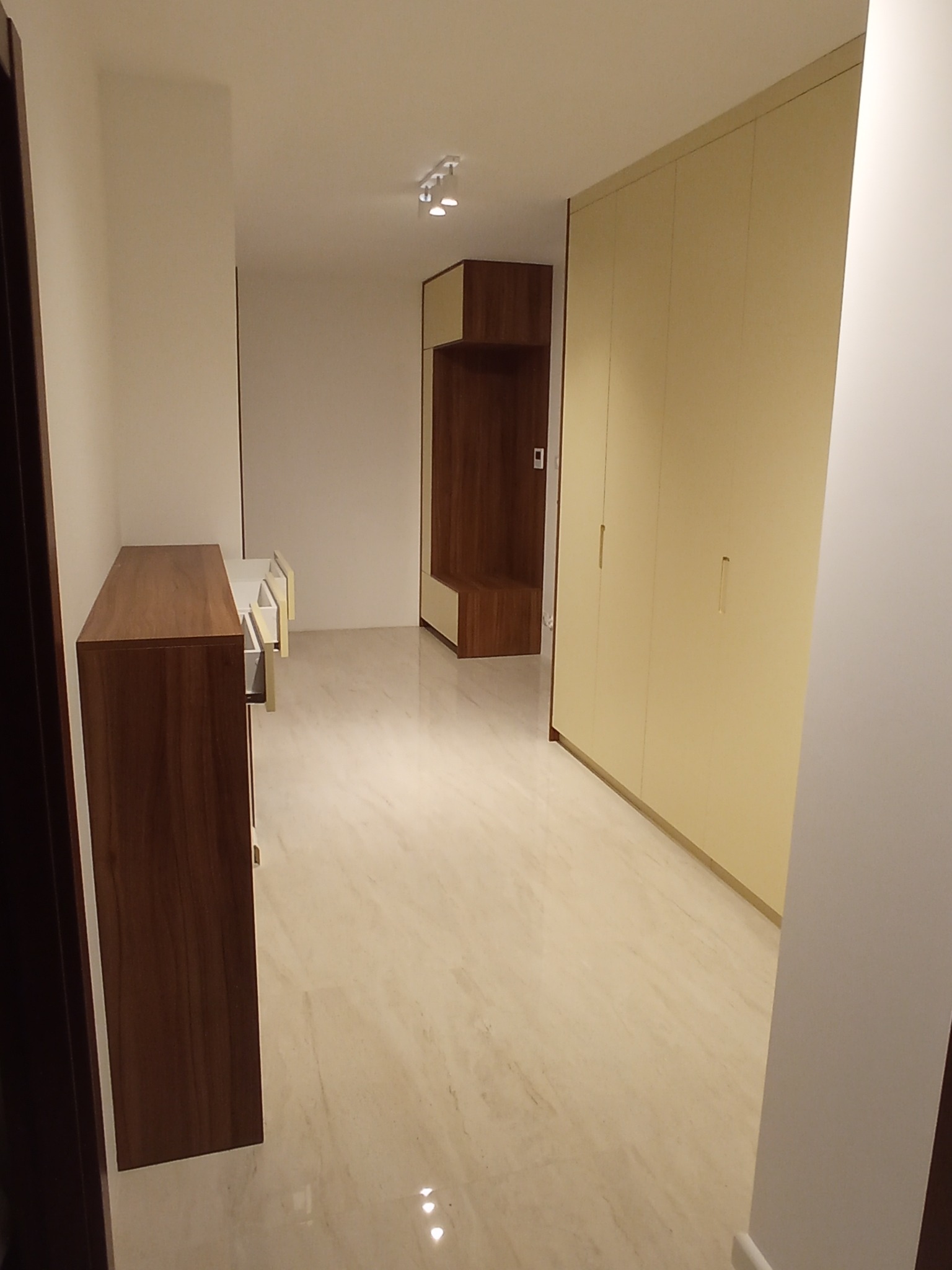 Wnętrze przedpokoju z drewnianą komodą z wysuniętymi szufladami, beżową szafą w zabudowie i marmurową podłogą.