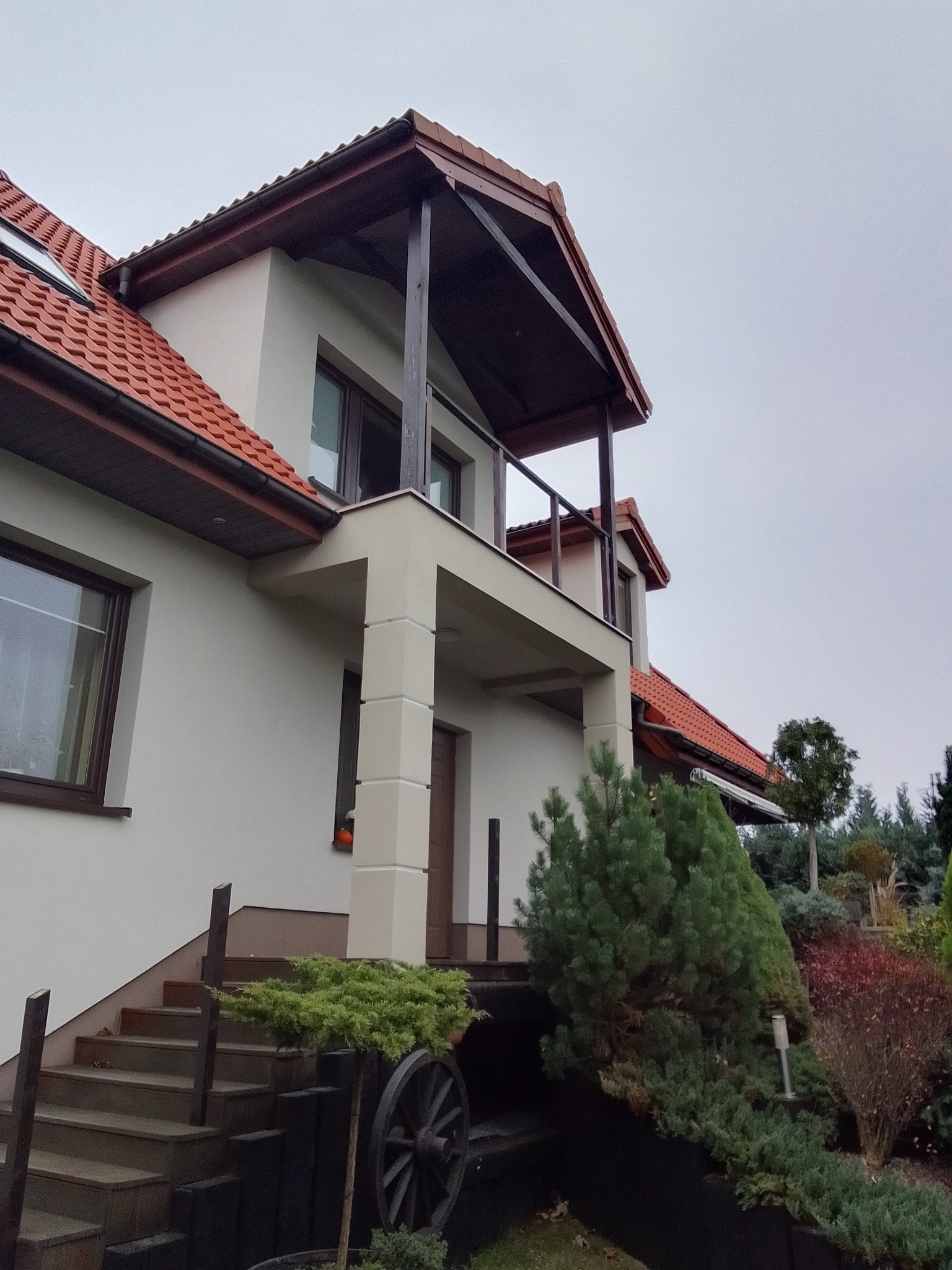 Ocieplony dom jednorodzinny z balkonem, widok z dołu na elewację, schody wejściowe i ozdobny wóz.
