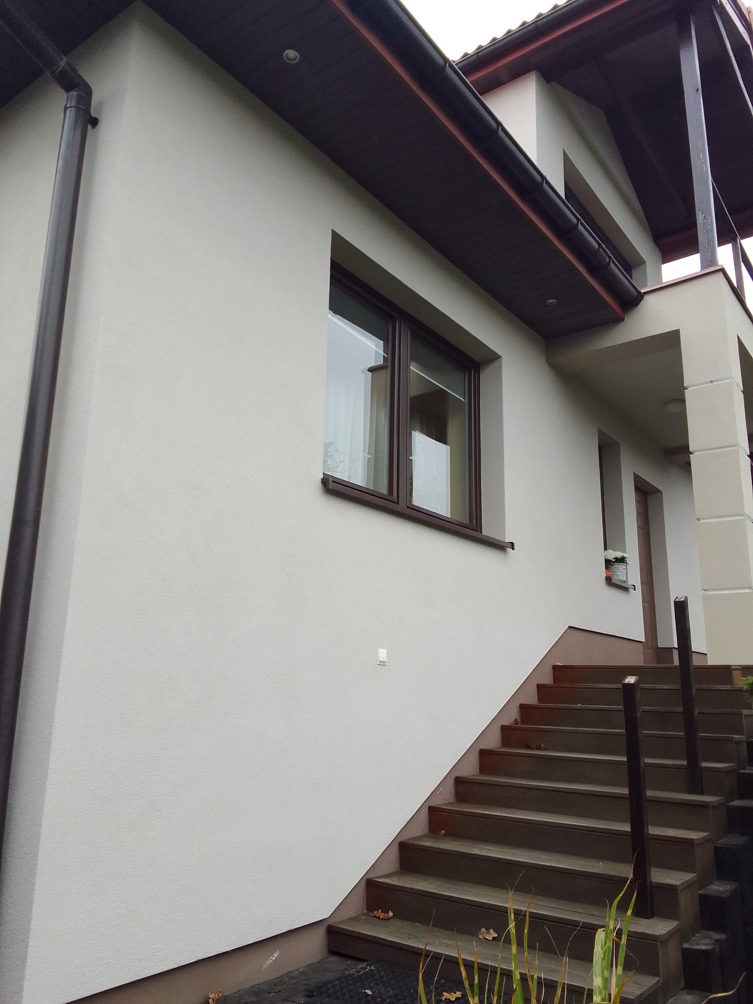 Jasna elewacja domu jednorodzinnego z brązowymi oknami i drewnianymi schodami wejściowymi, widok z dołu.