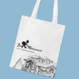 Biała torba bawełniana z czarnym nadrukiem logo hotelu i restauracji Jaś Wędrowniczek oraz szkicem budynku na błękitnym tle.