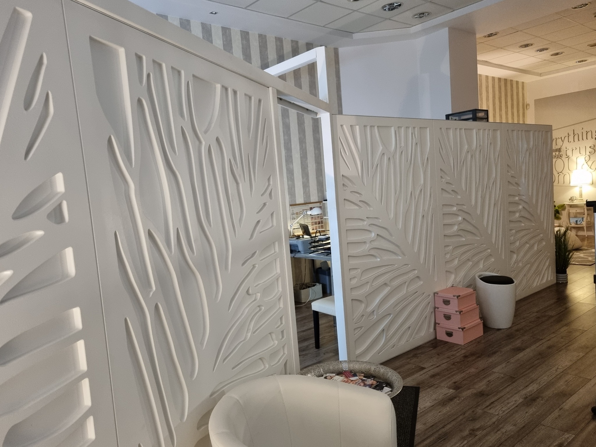 Nowoczesna poczekalnia z białymi ściankami działowymi o ażurowym wzorze, krzesłem i dekoracjami w jasnych kolorach.