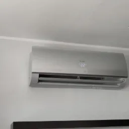 Zamontowany klimatyzator Haier w szarym kolorze na białej ścianie, z widocznym wyświetlaczem temperatury 22 stopnie, obok widoczny głośnik Technics i fragment lampy sufitowej.