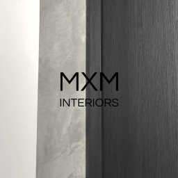 Mxm Interiors - Nowoczesne, grafitowe drzwi wewnętrzne z metalową klamką, na tle białej ściany i ściany z efektem betonu architektonicznego, z widocznym logo MXM Interiors.