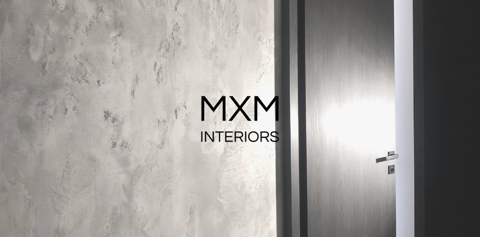 Ściana z efektem dekoracyjnym w odcieniach szarości, obok drewniane drzwi z nowoczesną klamką, widoczne logo MXM Interiors.