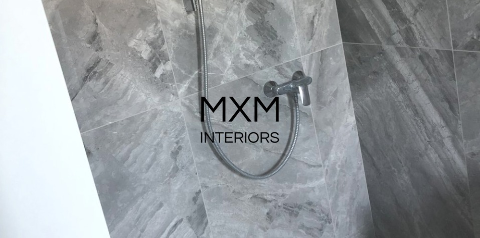 Szara marmurowa glazura ścienna z chromowaną baterią prysznicową i wężem, widoczne logo firmy MXM Interiors.