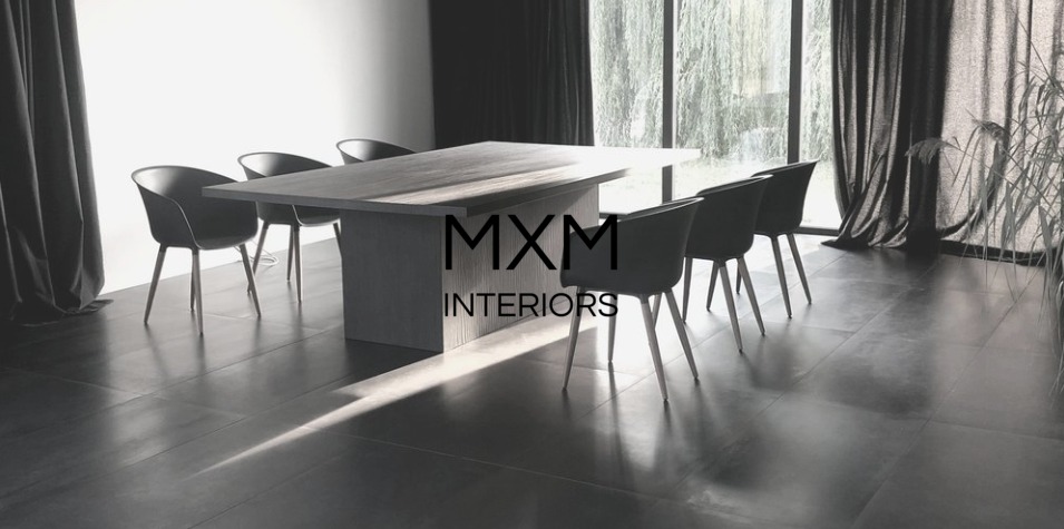 Minimalistyczna jadalnia w odcieniach szarości: duży stół z krzesłami na tle okna z zasłonami, ciemna podłoga z płytek, widoczny napis MXM Interiors.