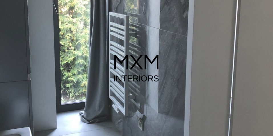 Nowoczesna łazienka z szarą, marmurkową płytką, białym grzejnikiem drabinkowym i oknem z widokiem na zieleń, zasłoniętym szarą zasłoną.