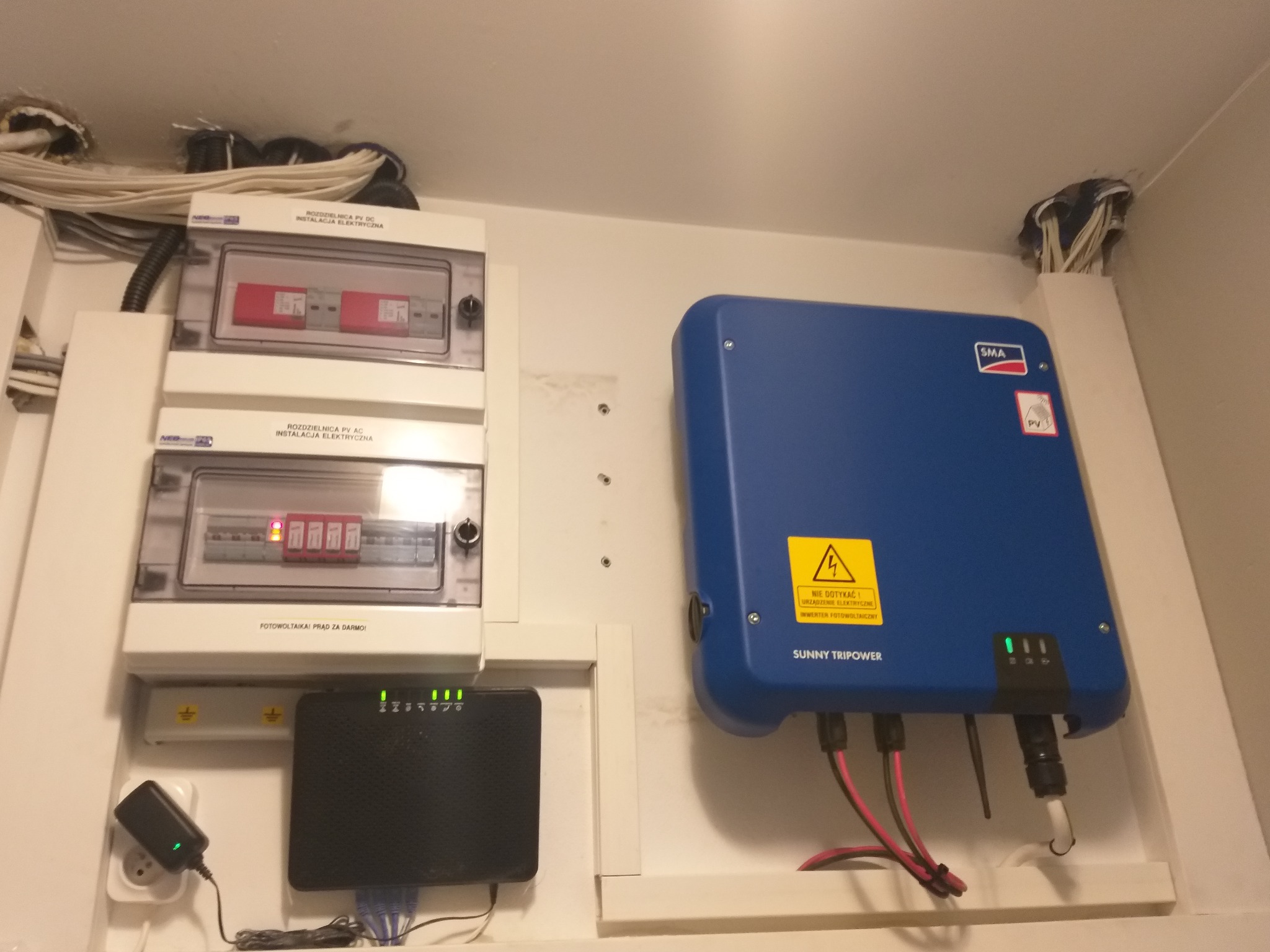 Rozdzielnica elektryczna z zabezpieczeniami nad inwerterem Sunny Tripower, widoczne okablowanie i podłączenie do sieci elektrycznej.