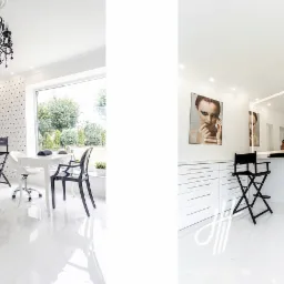 Jasne wnętrze salonu urody z krzesłem reżyserskim, białym stołem do manicure i dekoracyjnym oświetleniem, widok na ogród przez duże okno, minimalistyczny design.