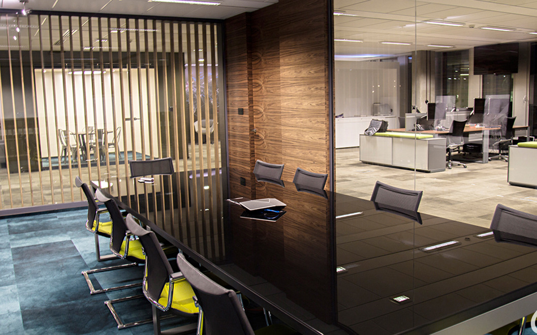 Nowoczesna sala konferencyjna z długim, czarnym stołem i krzesłami z żółtymi akcentami, widok na przeszkloną przestrzeń biurową z biurkami i krzesłami.