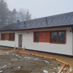 Nowoczesny dom jednorodzinny w Grodzisku z drewnianą stolarką okienną i częściowo wykończoną elewacją, widok z zewnątrz w pochmurny dzień.