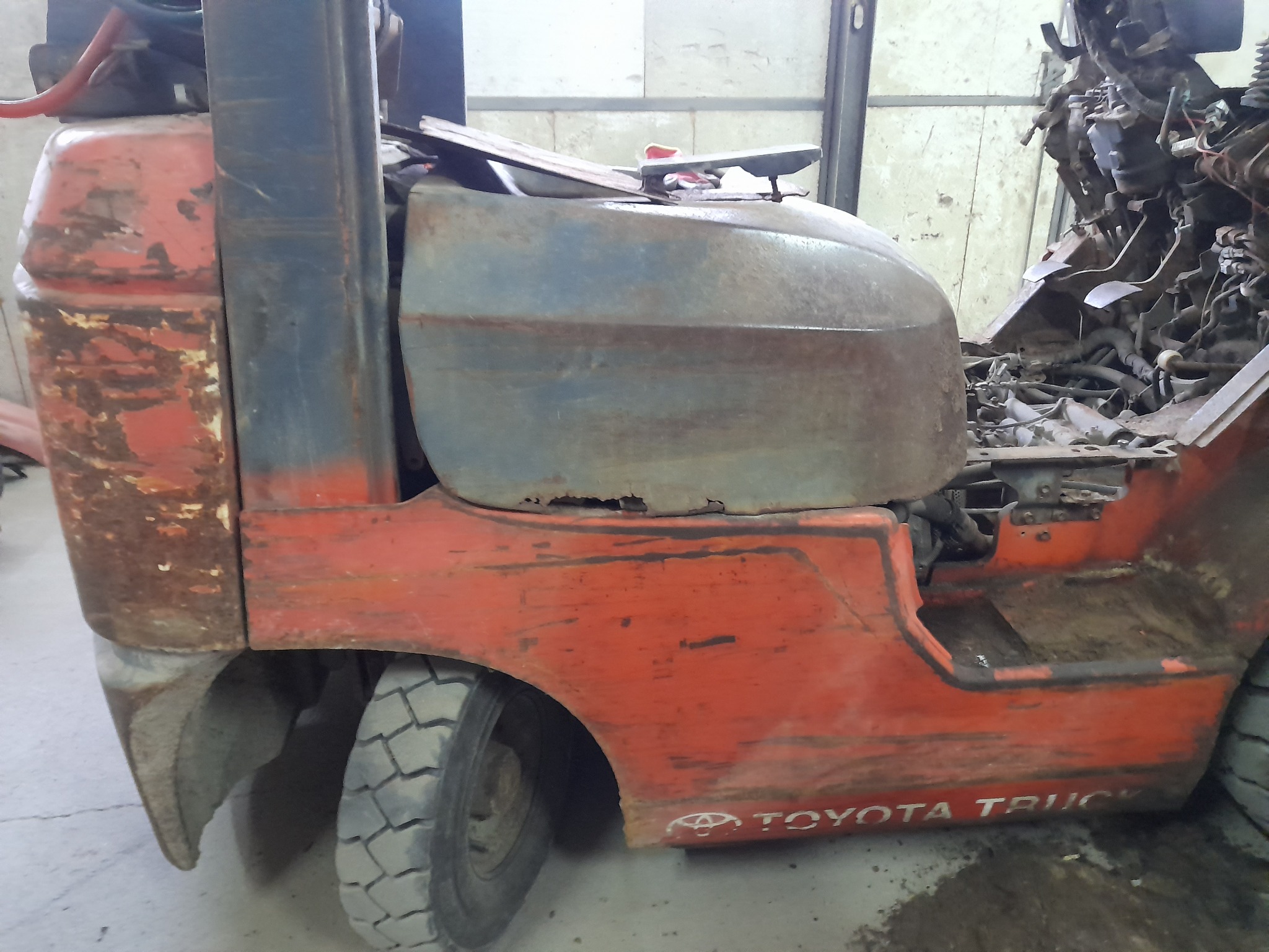 Częściowo rozebrany, zardzewiały wózek widłowy Toyota Truck w warsztacie, widoczne elementy silnika i karoserii z licznymi śladami korozji.