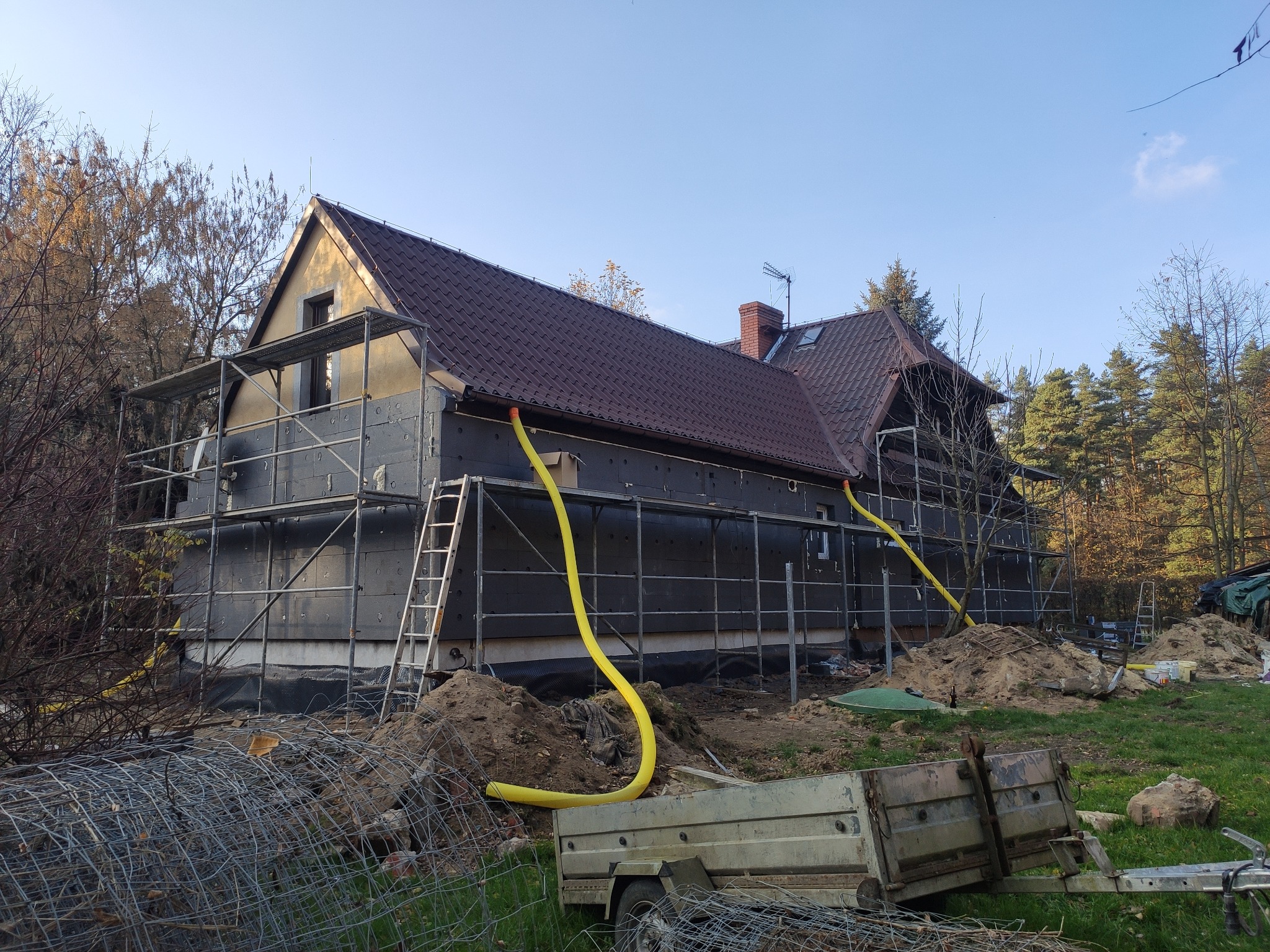 Dom w trakcie ocieplania, widoczne rusztowania, żółte węże wentylacyjne i przygotowane materiały izolacyjne na elewacji zewnętrznej.