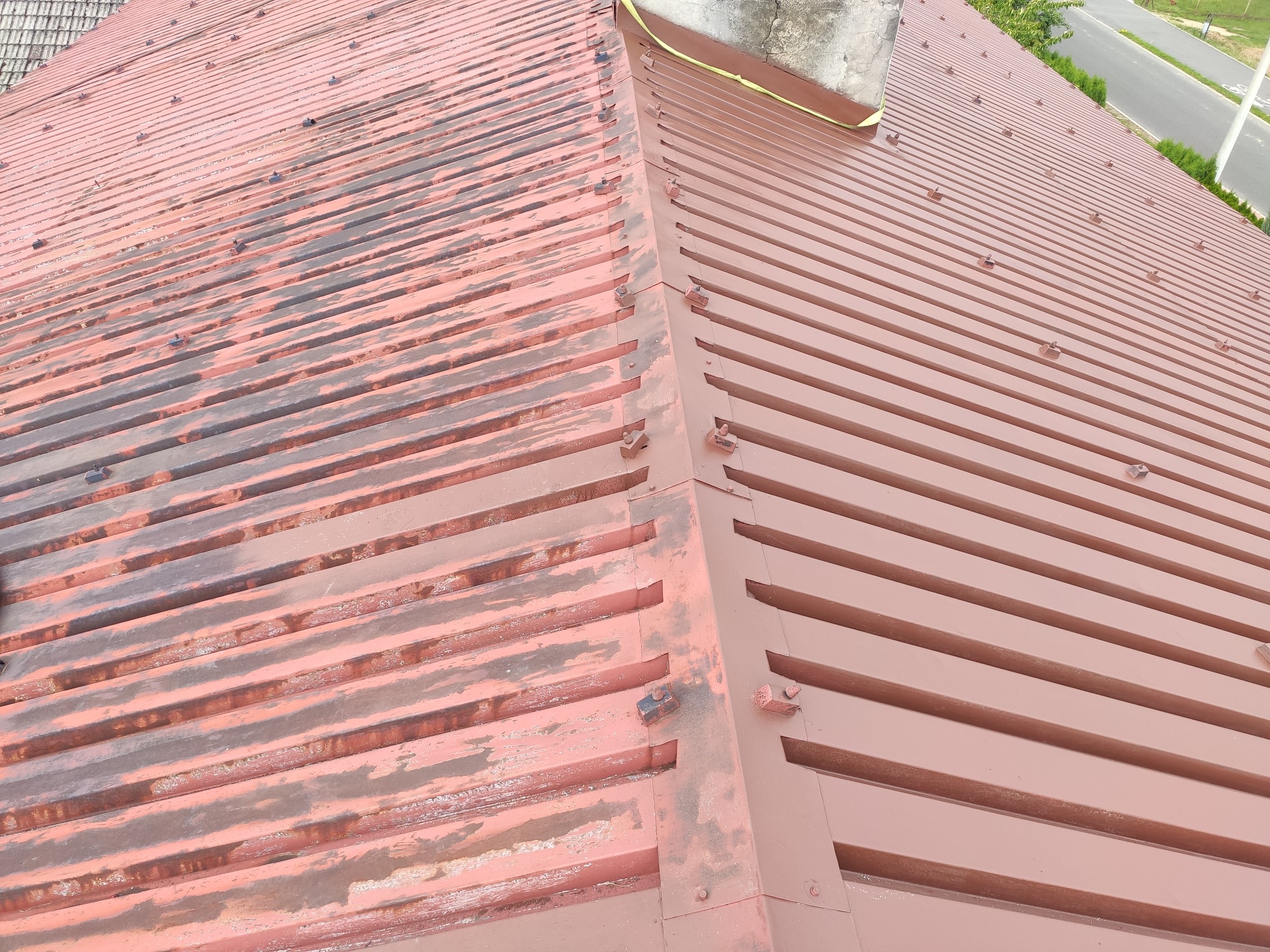 Częściowo odnowione, pomalowane blaszane pokrycie dachowe w kolorze ceglastym; widoczna różnica w kolorze między starą a nową powłoką.