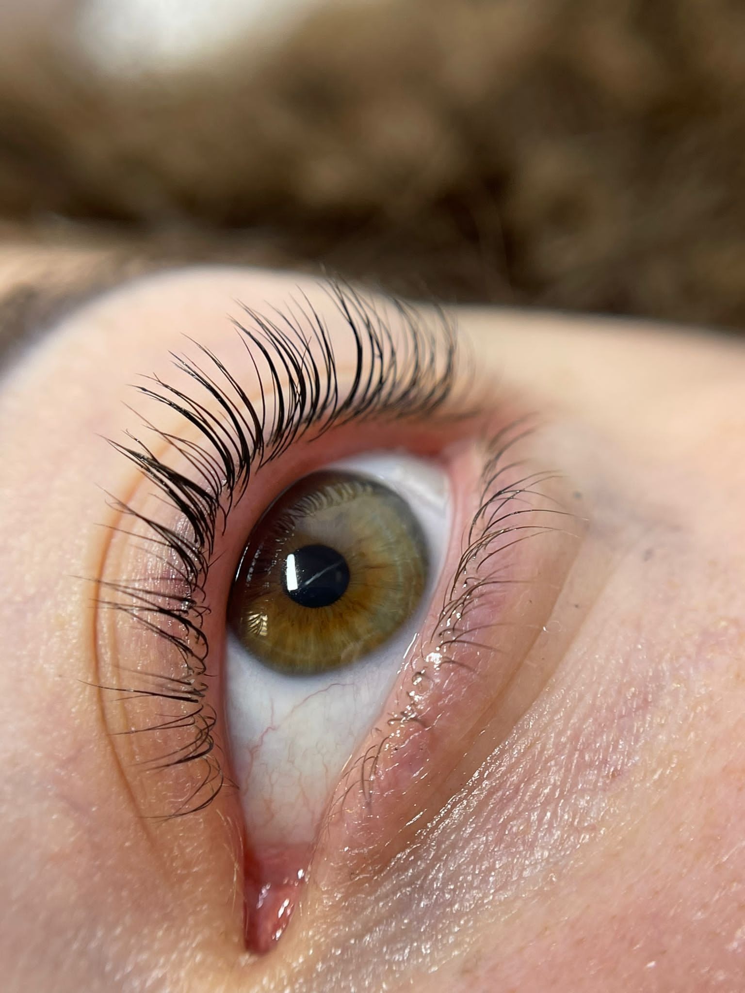 Zbliżenie na oko z przedłużonymi, czarnymi rzęsami, widoczne delikatne zaczerwienienie w kąciku oka i odbicie światła w tęczówce.