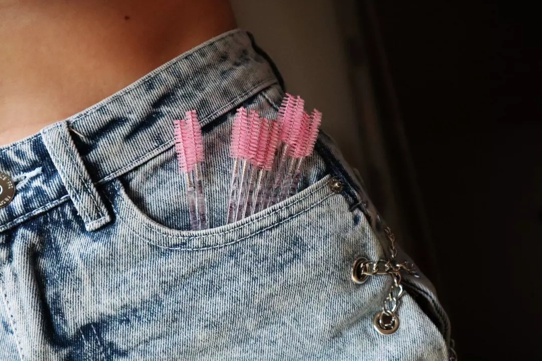 Zbliżenie na dżinsową kieszeń spodni z 6 różowymi szczoteczkami do rzęs, ozdobiona łańcuszkiem.