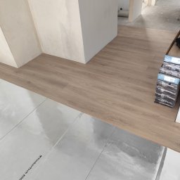 M&E Invest Sp z o.o. usługi elektryczne i glazurnicze - Układanie paneli podłogowych na folii izolacyjnej, widoczne paczki paneli Berry Alloc, fragment ściany w tle. Etap prac wykończeniowych.