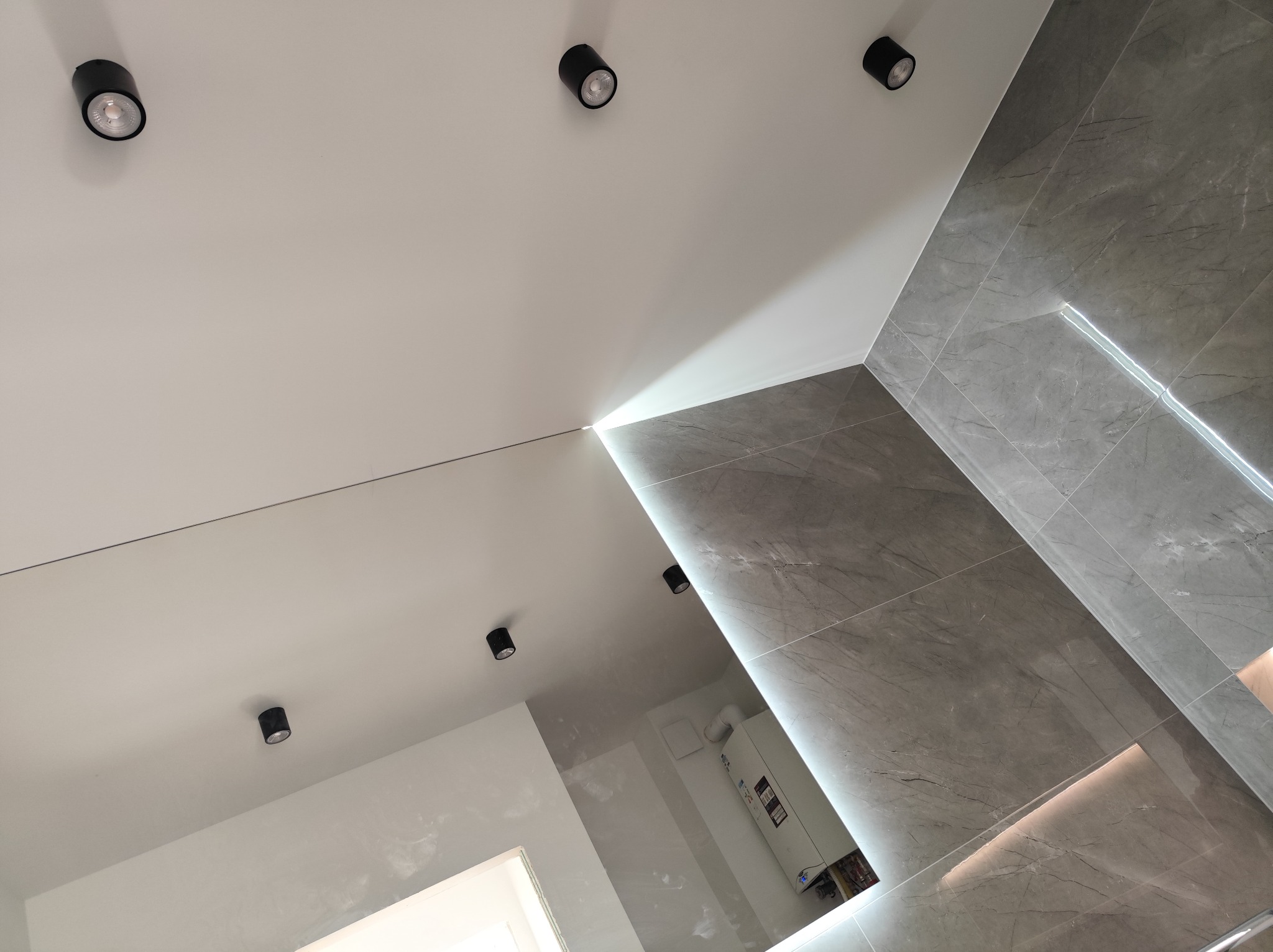 Nowoczesna łazienka po remoncie: szare płytki imitujące marmur, podświetlenie LED w narożniku, biały sufit z czarnymi reflektorami punktowymi.
