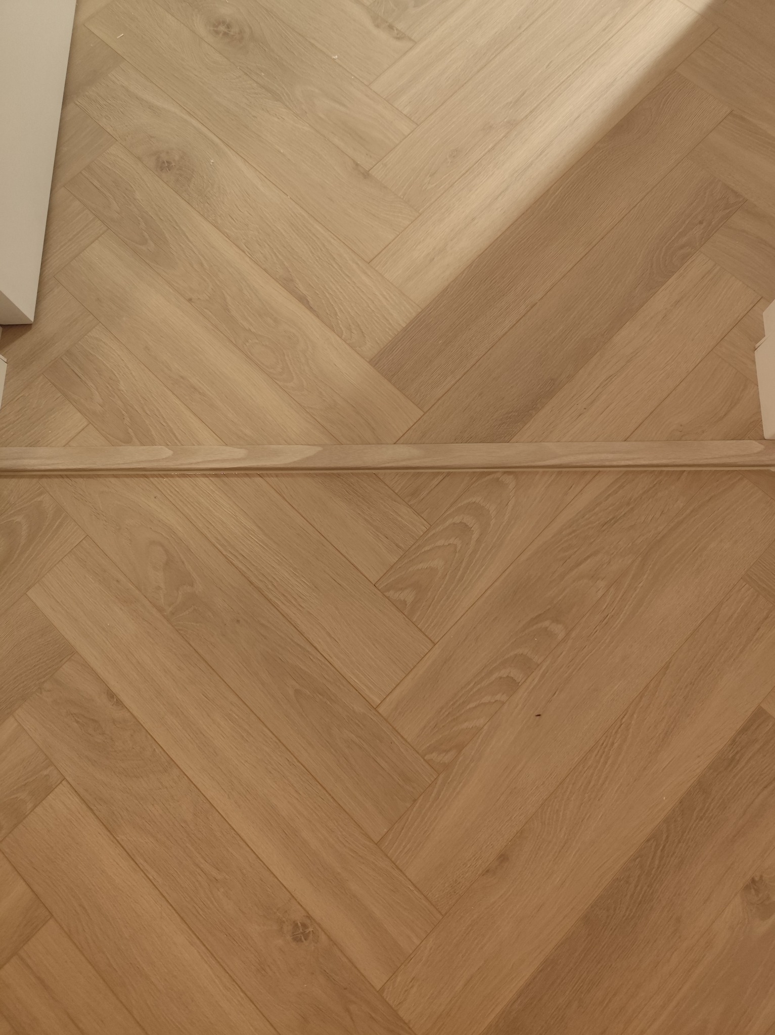 Parkiet ułożony w jodełkę francuską, z widoczną listwą przypodłogową. Jasne drewno, naturalne usłojenie. Ujęcie z góry, fragment wykończonego wnętrza.