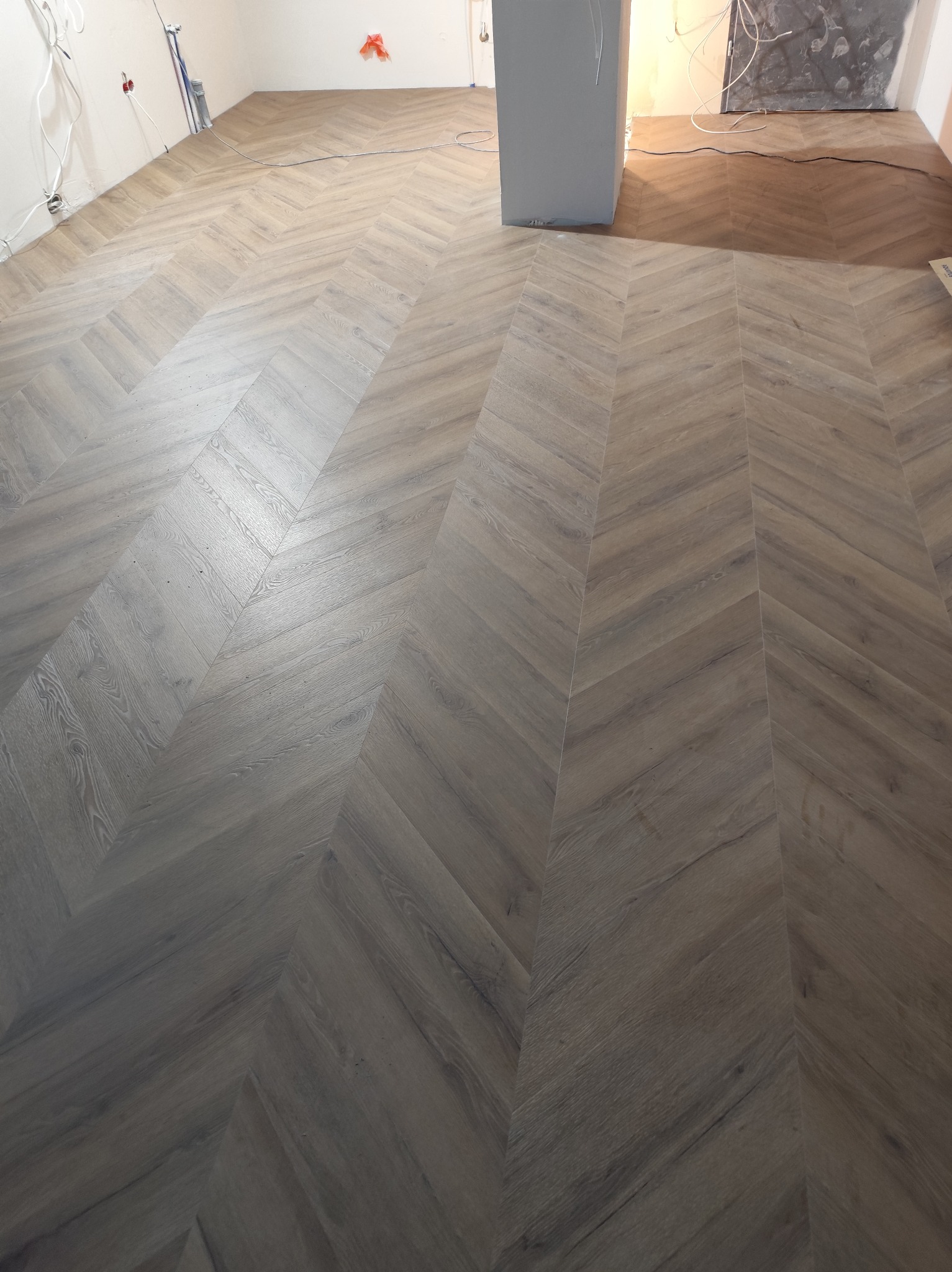 Ułożona podłoga z paneli w jodełkę, jasne drewno, widoczne kable i instalacje na ścianach, surowy stan wykończenia wnętrza, detale układania paneli.